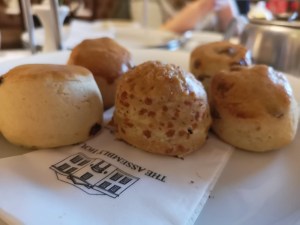 A row of scones of a cake stand. There is a white napkin underneath them with the Assembly House logo on in black. 