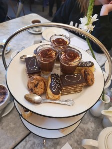 Looking down onto the top tier of the cake stand. You can see four different desserts. A cookie, an eclair, a shot glass and a gateau. 