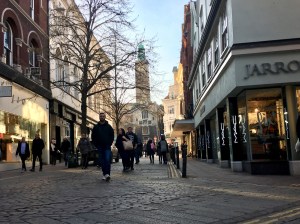 An image looking down one of the streets in Norwich. You can see the cobblestone pathway. The City Hall clock is in the distance.