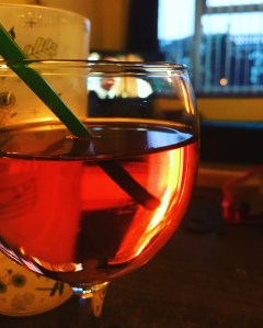 A glass of rosé wine with a straw. You photo is taken in candlelight and the wine is glowing. 