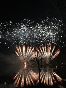 A mirror image of red fireworks in the sky and on the water of the lake. 