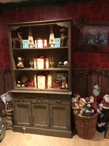 A large bookcase filled with books a decorations. A basket full of gifts. The wallpaper is red. 