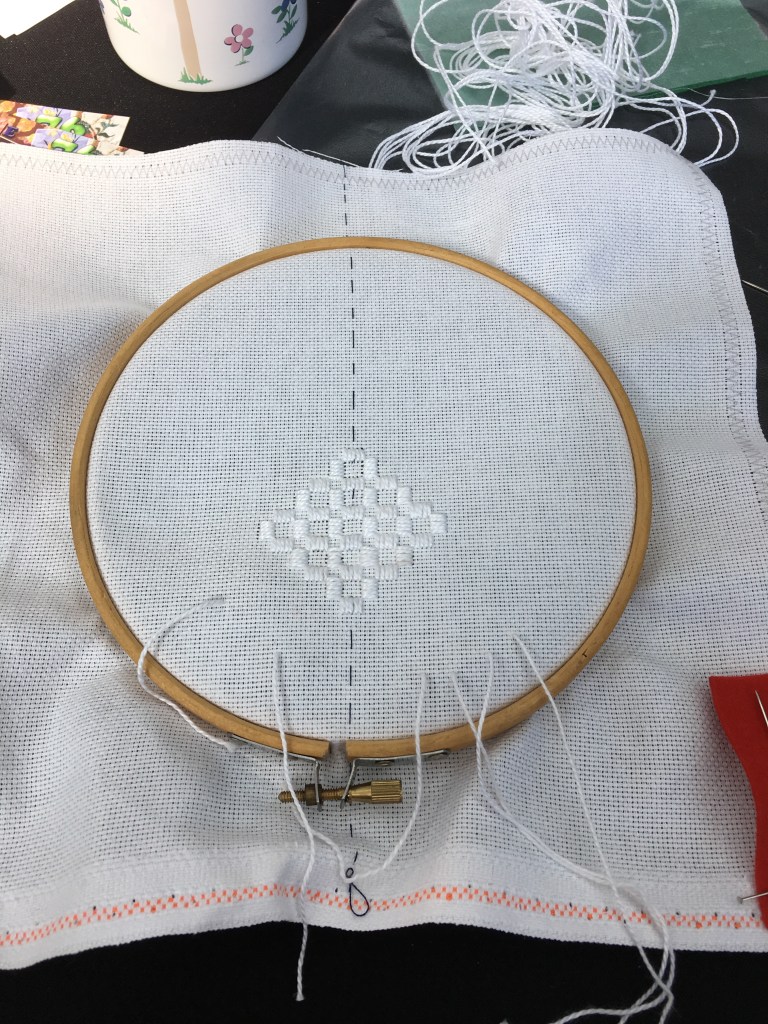 An embroidery hoop with white fabric inside. There is the beginnings of a pattern being stitched in white thread. 