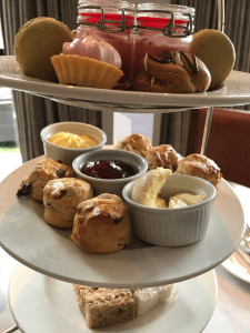 A close up of the afternoon tea stand, focussing on the scones. There a six mini scones with pots of cream, jam and butter. 