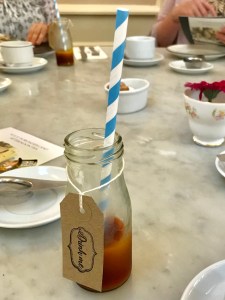 A small bottle half full of dark red liquid. A white and blue striped straw is in the bottle. A brown label reads Drink Me. 