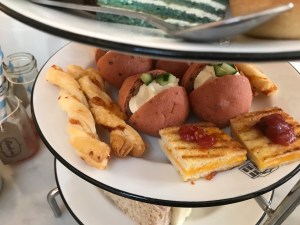 A photo showing the middle tier. Cheese straws on the left, pink brioche rolls in the middle and mini cheese toasties topped with chutney on the right. 