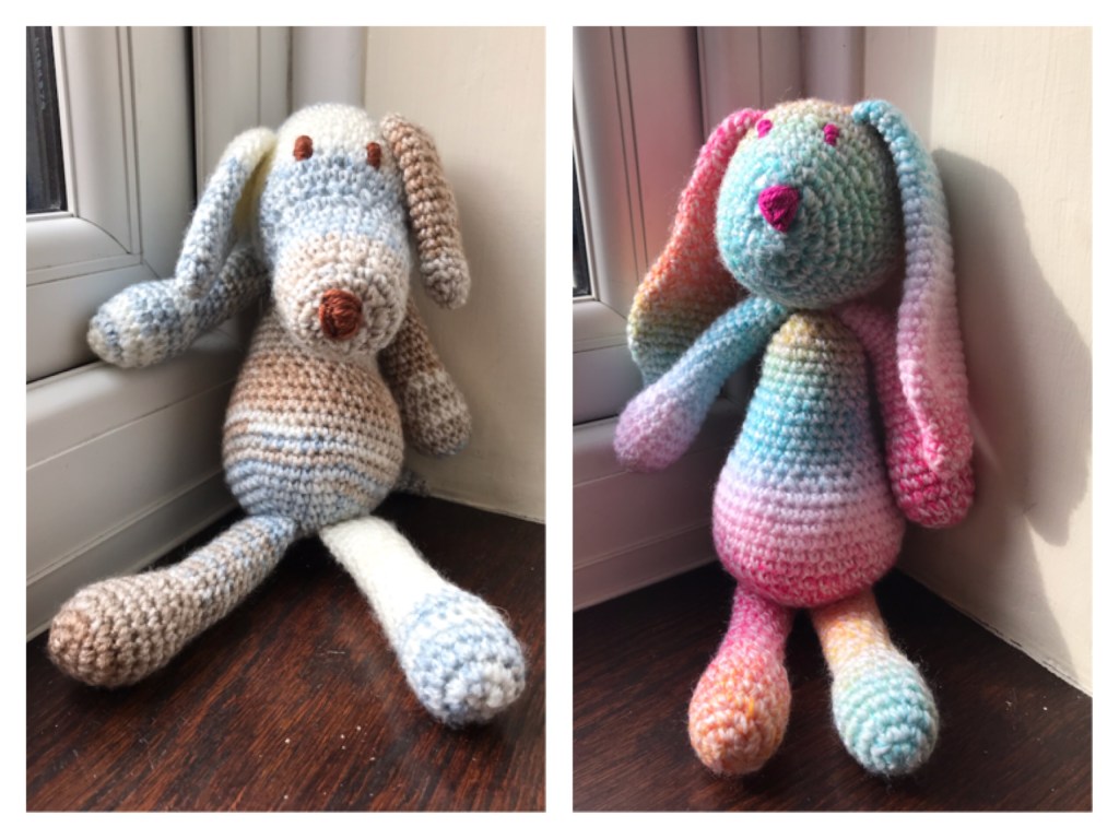 On the left is a stuffed crochet dog in blue brown and white graduated wool. On the right is a crochet bunny using multicoloured rainbow stripy wool. It has big long ears. 