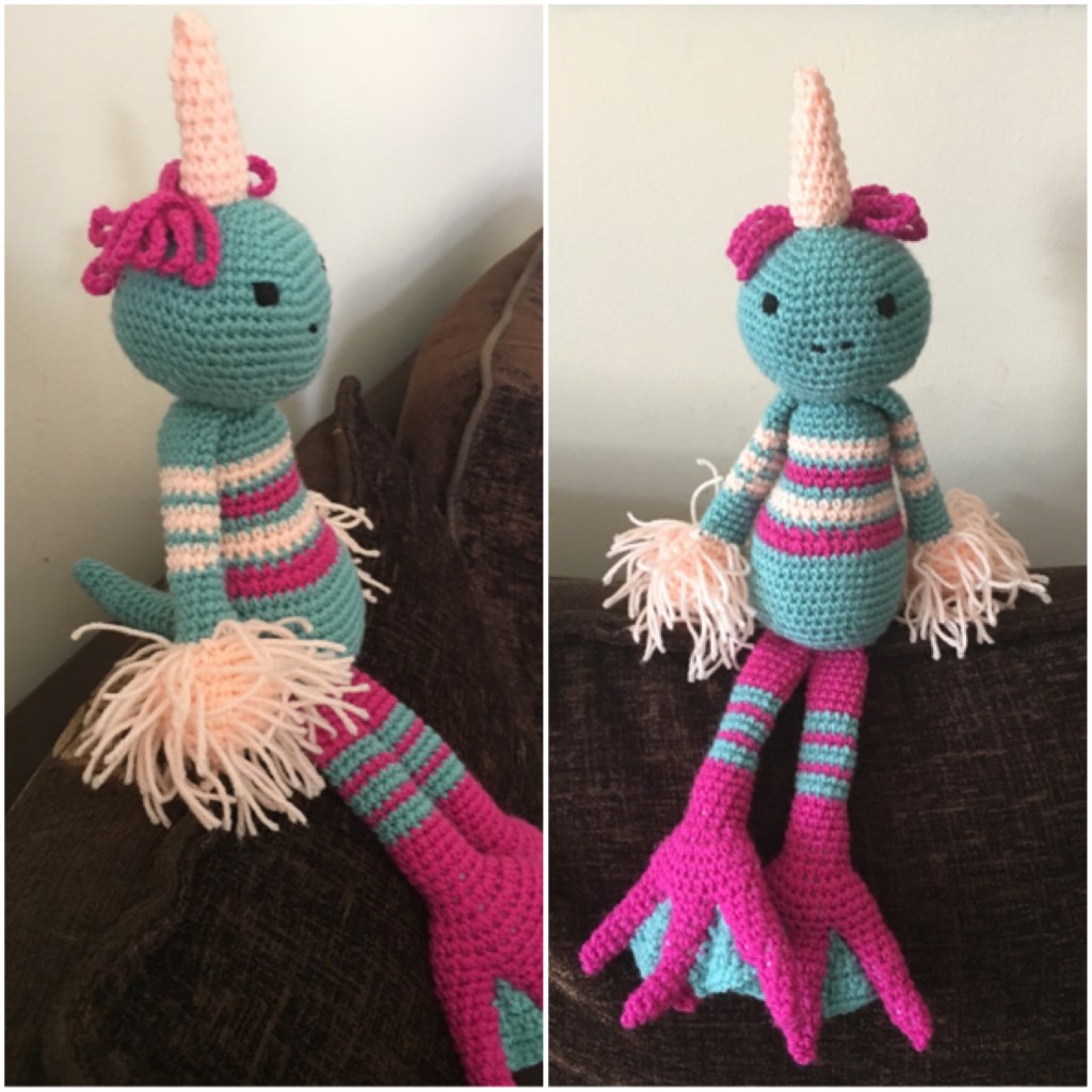 The monster unicorn design from two different angles. The main body is light blue and he has pink and white stripes. The legs are pink with duck style feet. He has fluffy peach hands and a horn on his head with tufts of pink curly hair.