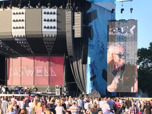 Caswell are on stage. On the screen to the right of the stage is the female lead singer. The backdrop to the stage is red with Caswell written on.