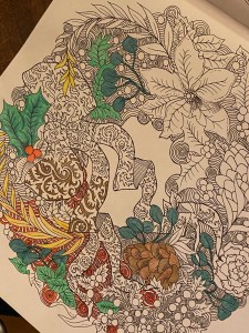 A partly coloured in Christmas wreath. There is holly, leaves, pine cones and swirls. 