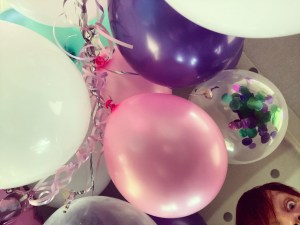 Pink white and purple balloons, some filled with confetti sequins. The top of my face and red hair can be seen peeking in the bottom right corner. 