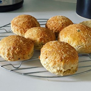 Six golden looking cheese scones that haven’t risen very much. They are on a cooling rack on a white kitchen surface.