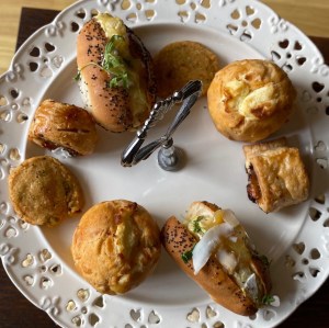 A photo looking down onto the savoury bites. There are two of each. Sausage roll, filled bridge roll, cheese biscuit and muffin. 