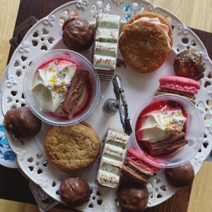 A photo looking down onto the top tier of cakes. There are two of each cake that will be detailed below. One is gateau, a macaron, a potted dessert and a cookie. 