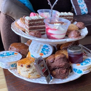 A side on photo of the two tiered cake stand with all sweet items on. The cakes mentioned above, along with chocolate truffles and chocolate scones. 