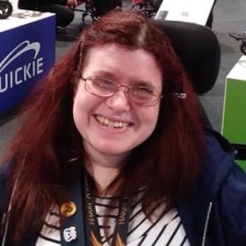 A portrait photo of Emma. Head and shoulders shot. Emma has dark red hair that is long and styled down, a black and white strip top and is wearing glasses. 