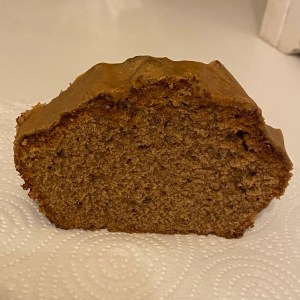 A slice of loaf cake in a golden brown caramel colour. It’s sponge cake with a layer of icing on top. It’s placed on a white surface.